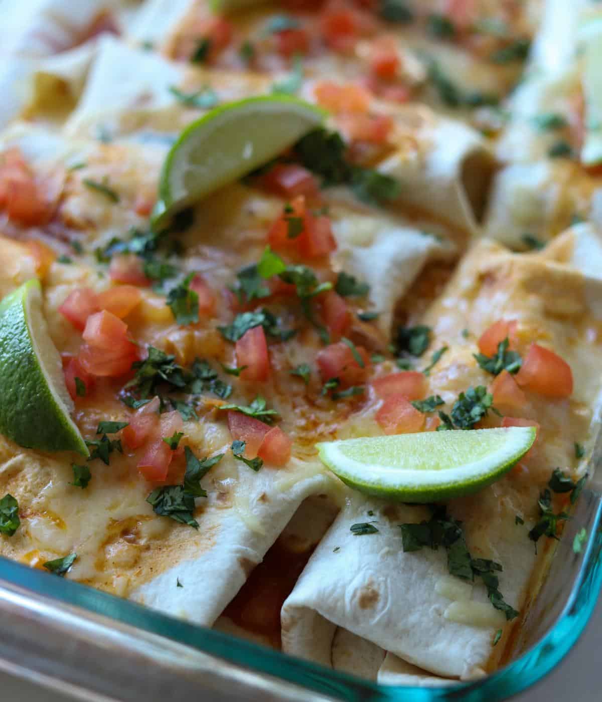chicken enchiladas baked in dish topped with cheese, tomato, cilantro and lime