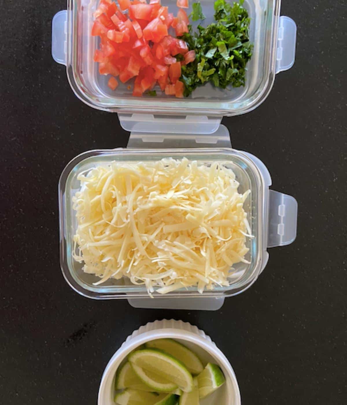 two dishes filled with tomato, cilantro, and cheese with one bowl full of limes.