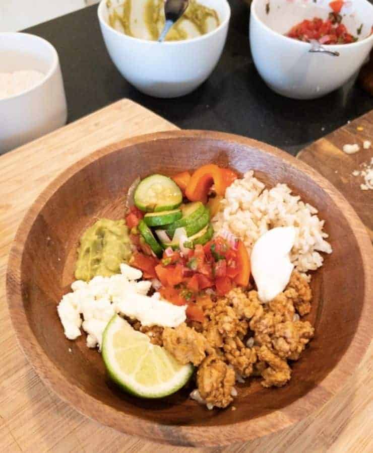 turkey taco bowl filled with rice zucchini feta sour cream and lime with bowl of pico de gallo and quacamole