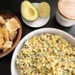Corn Salad in large bowl with tortilla chips and avocado and lime on the side