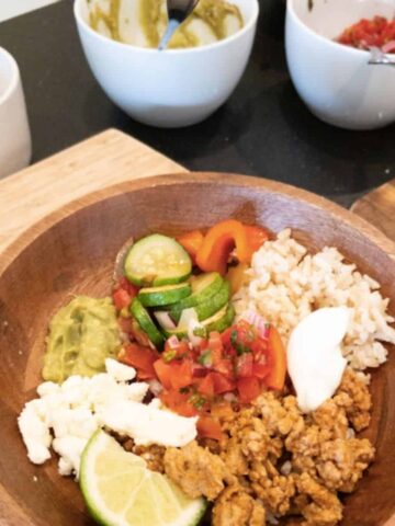 turkey taco bowl with toppings in a wood bowl with pico de gallo and guacamole in white bowls