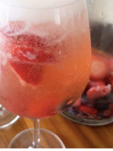 wine glass with summer sangria and pitcher in background with fresh berries and sangria