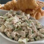 traditional chicken salad recipe in white bowl with croissants in background