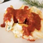 Vegetarian Stuffed Shells on a white plate covered with marinara sauce with rosemary garnish in background