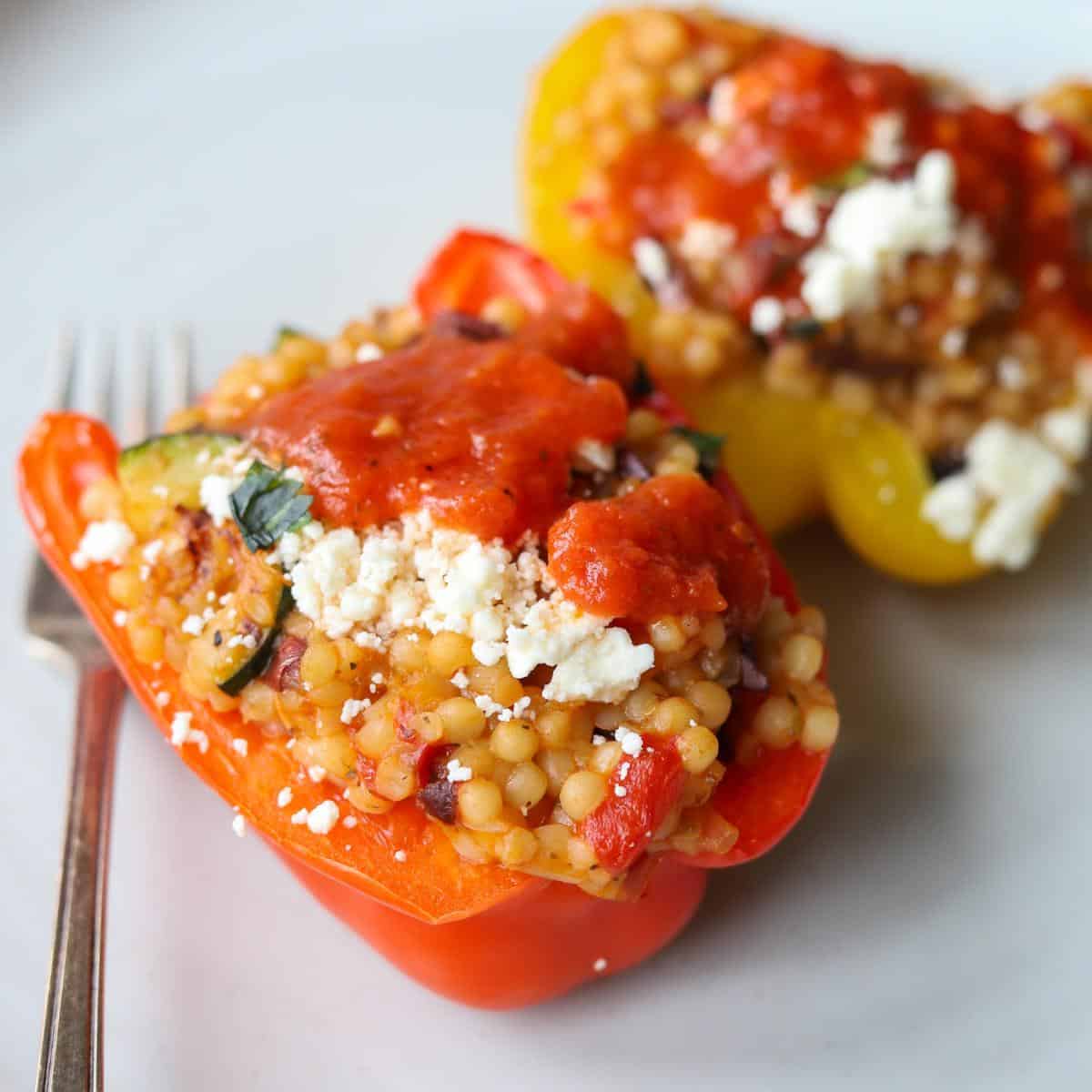 two couscous stuffed bell pepper on place topped with feta and marinara sauce