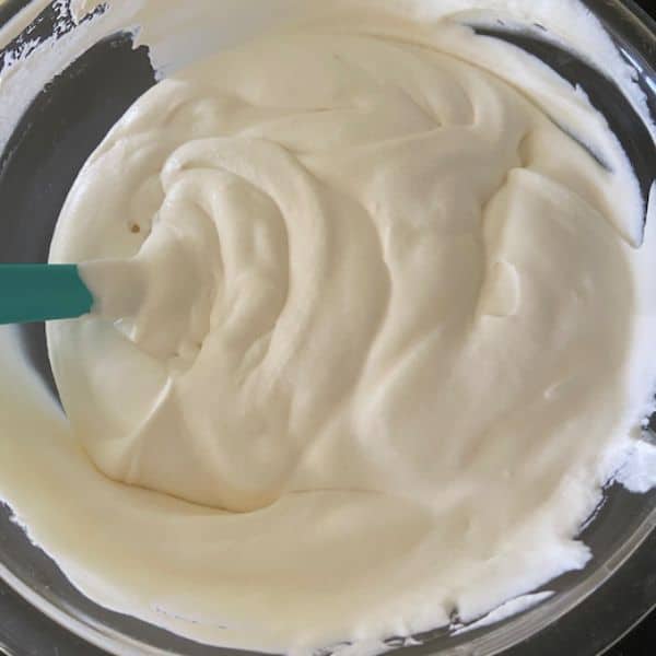 whipping cream folded into sweetened condensed milk mixture in glass bowl