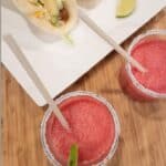 Two frozen watermelon margaritas with salt and lime on rim and tacos on plate