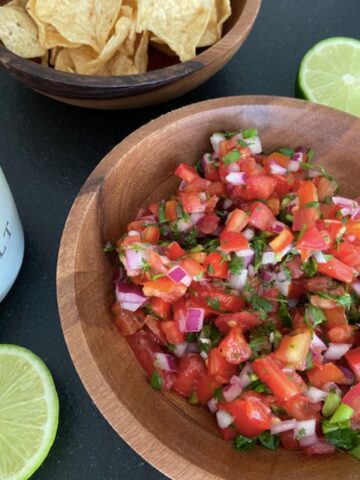 wooden bowl full of homemade pico de gallo with tortilla chips on the side and salt and lime