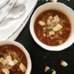 minestrone soup in bowls on black granite with croutons and parmigiano reggiano cheese sprinkled around