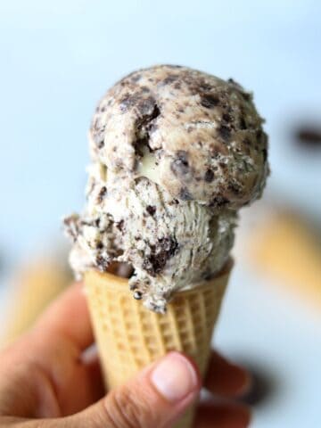 hand holding sugar cone topped with two scoops of oreo ice cream