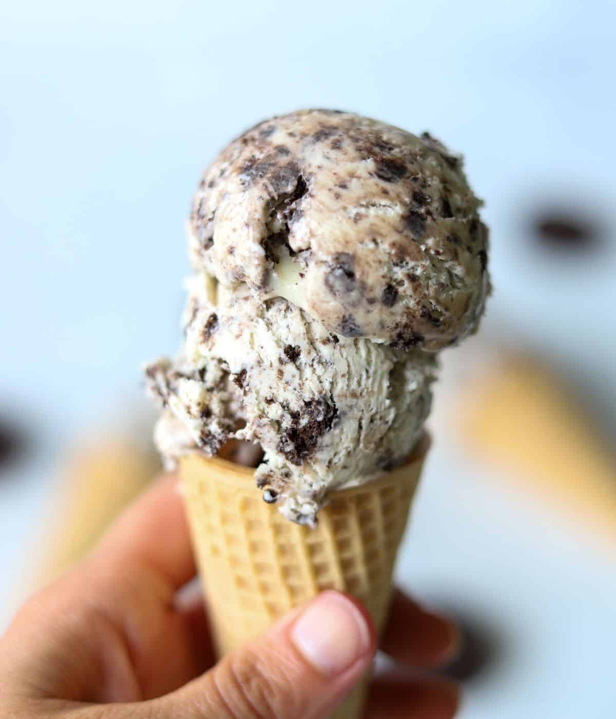 hand holding sugar cone topped with two scoops of oreo ice cream