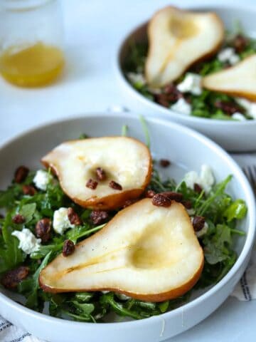 Roasted pear salad in white bowl with honey vinaigrette in jar.