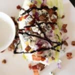 steakhouse wedge salad covered with blue cheese and balsamic glaze on white plate