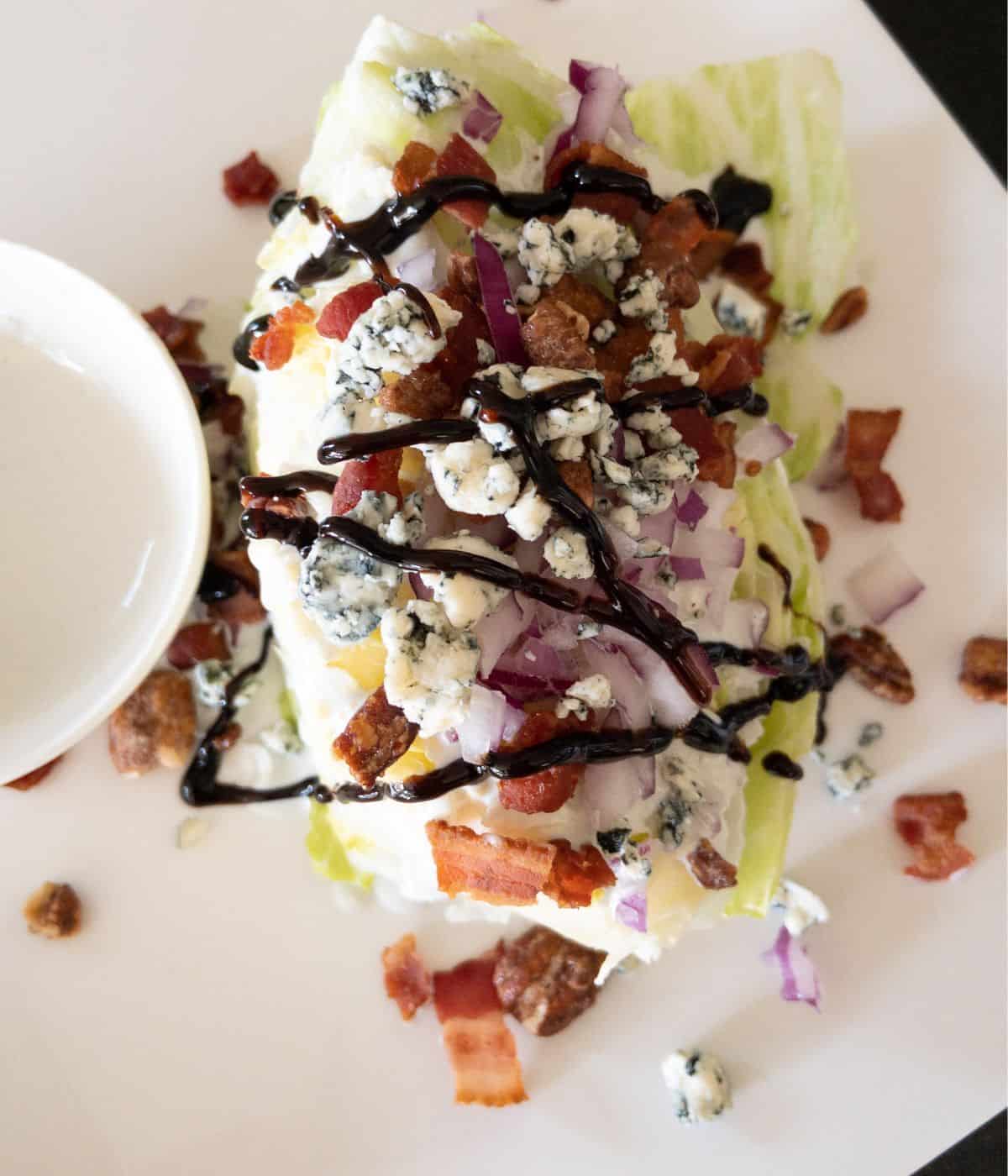 steakhouse wedge salad covered with blue cheese and balsamic glaze on white plate