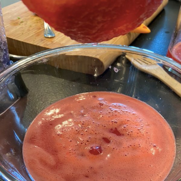 straining watermelon juice with large mesh strainer over glass bowl