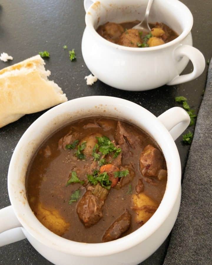 beef stew in soup bowl with french bread on table 