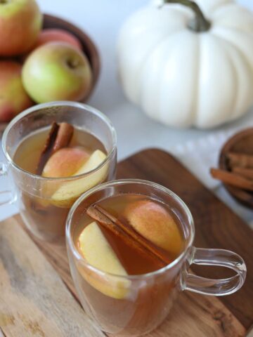Two hot apple cider bourbons topped with fresh apple and cinnamon sticks.
