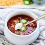 Dutch oven chili in bowl topped with sour cream, cheese and jalapeno