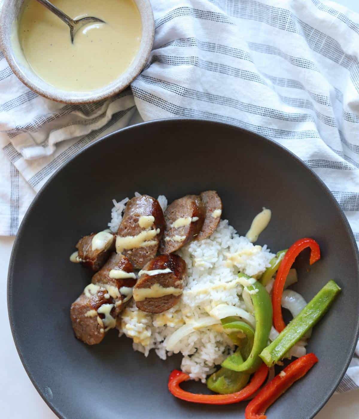 Bowl full of rice, peppers and onions and sausage with mustard aioli drizzle.