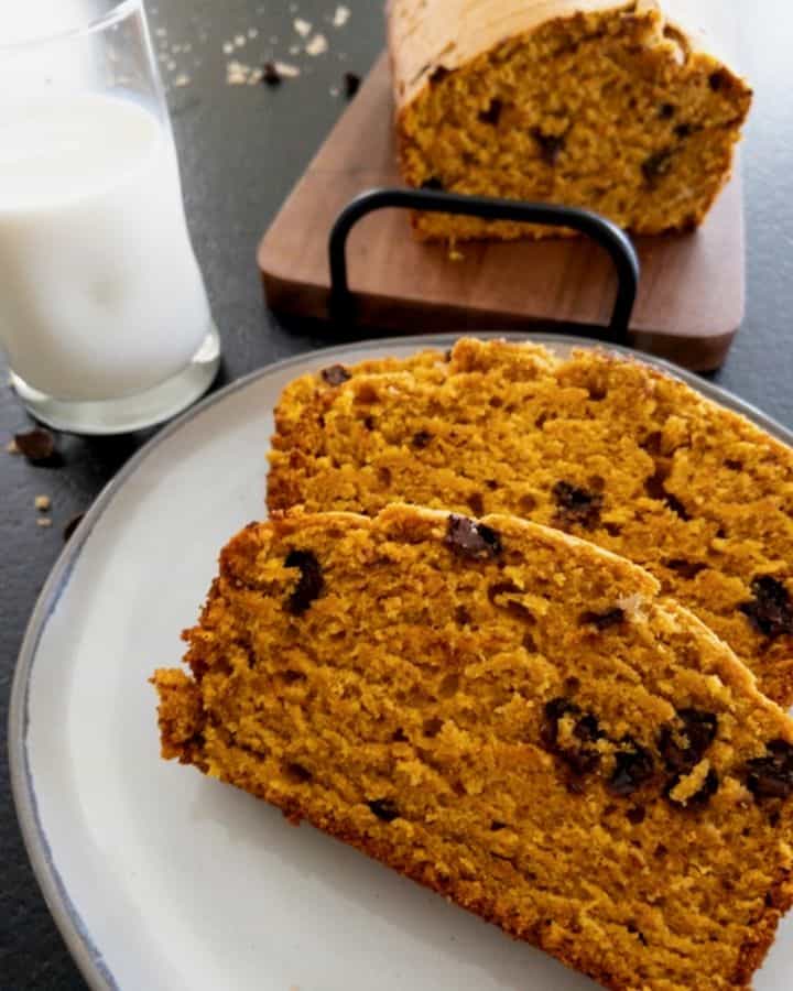 Pumpkin bread sliced on a stoneware plate with a glass of milk in background