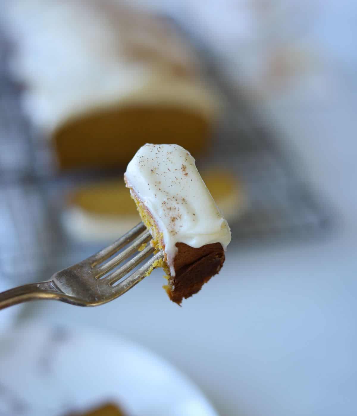 fork holding a bite of pumpkin bread with cream cheese frosting