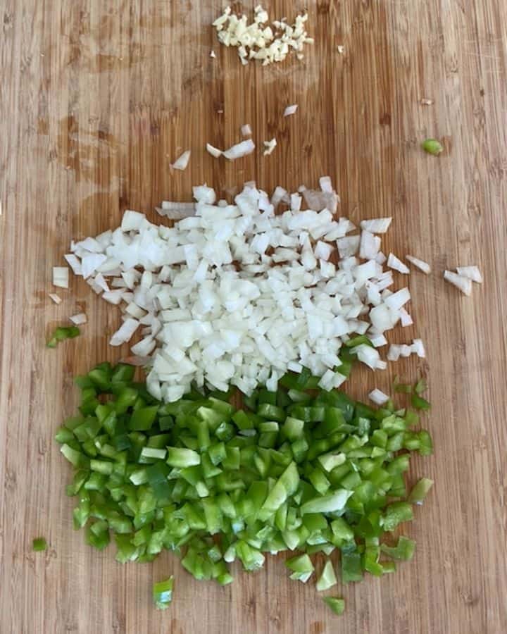 minced garlic and chopped green peppers and onion on cutting board