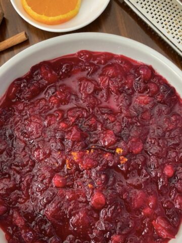 serving bowl of cranberry sauce with side of oranges, cinnamon stick and zester