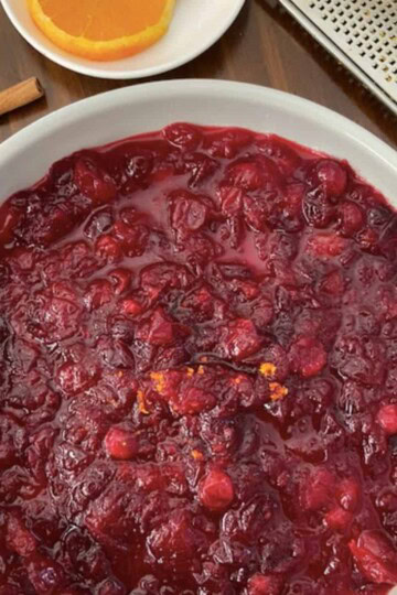 serving bowl of cranberry sauce with side of oranges, cinnamon stick and zester