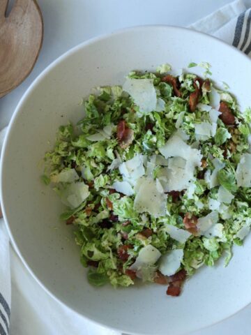 Shaved brussel sprout salad in salad bowl topped with parmesan cheese.