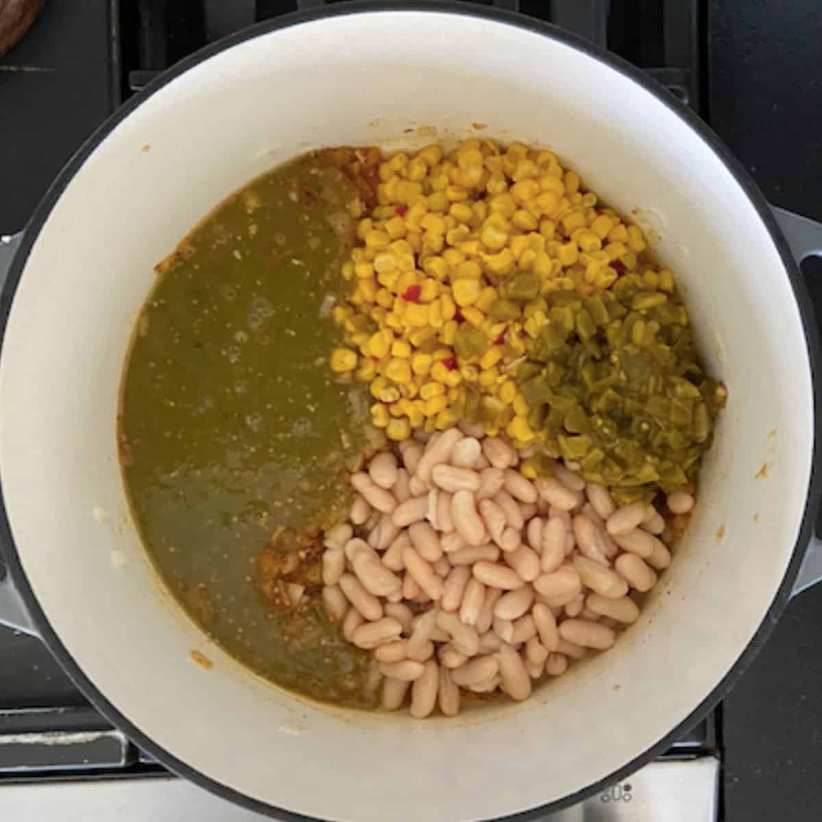 Cans of green chiles, beans, corn, and chile verde added into dutch oven.