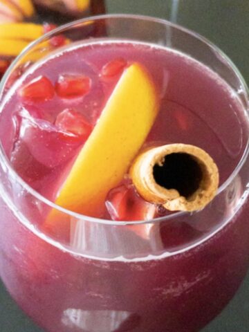 wine glass full of cranberry sangria topped with orange slice cinnamon stick and pomegranate arils