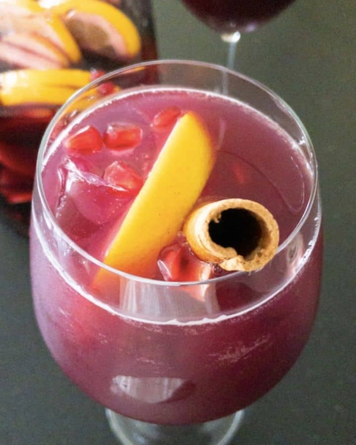 wine glass full of sangria topped with orange slices, pomegranate arils, and cinnamon stick