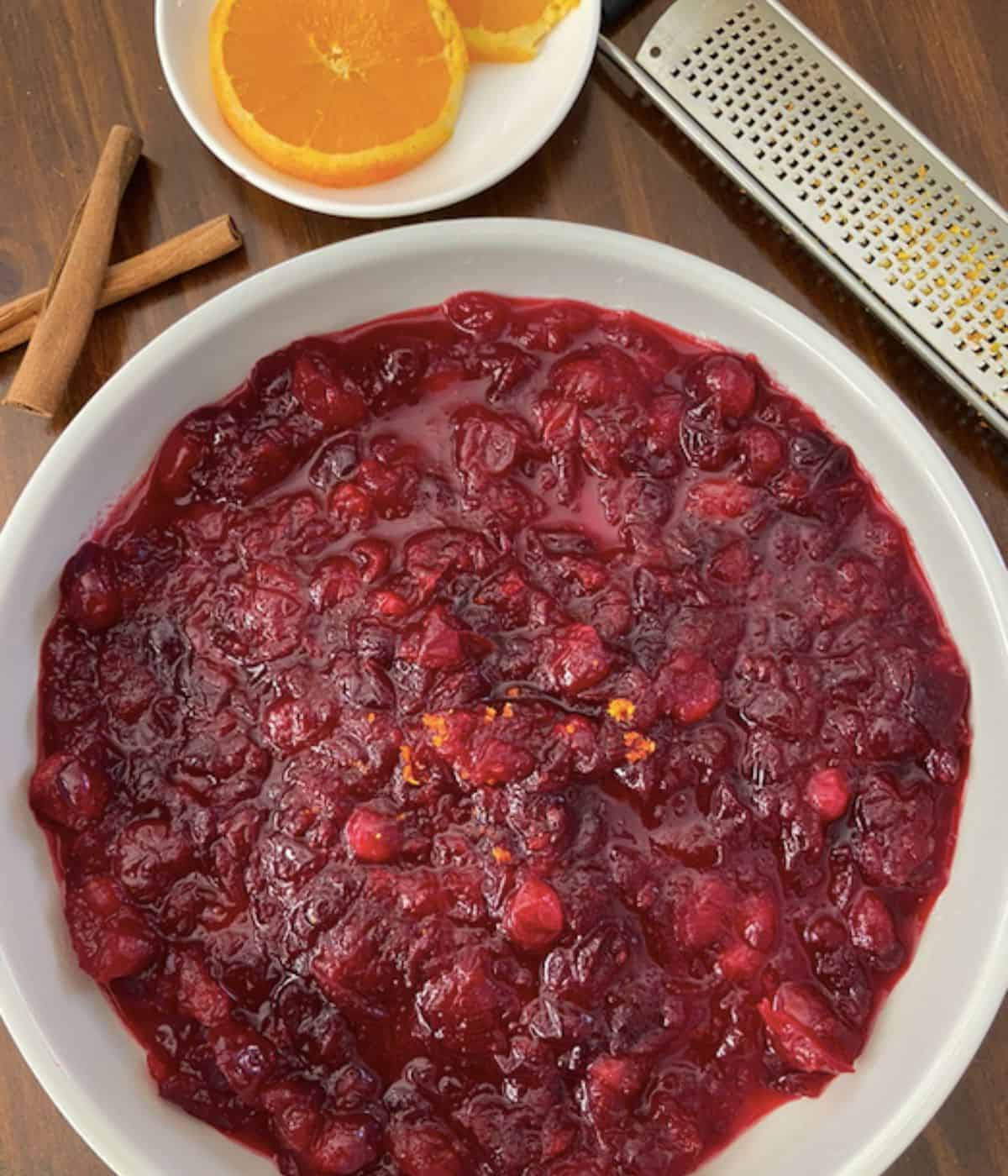 large bowl of cranberry sauce with orange slices on the side and cinnamon sticks