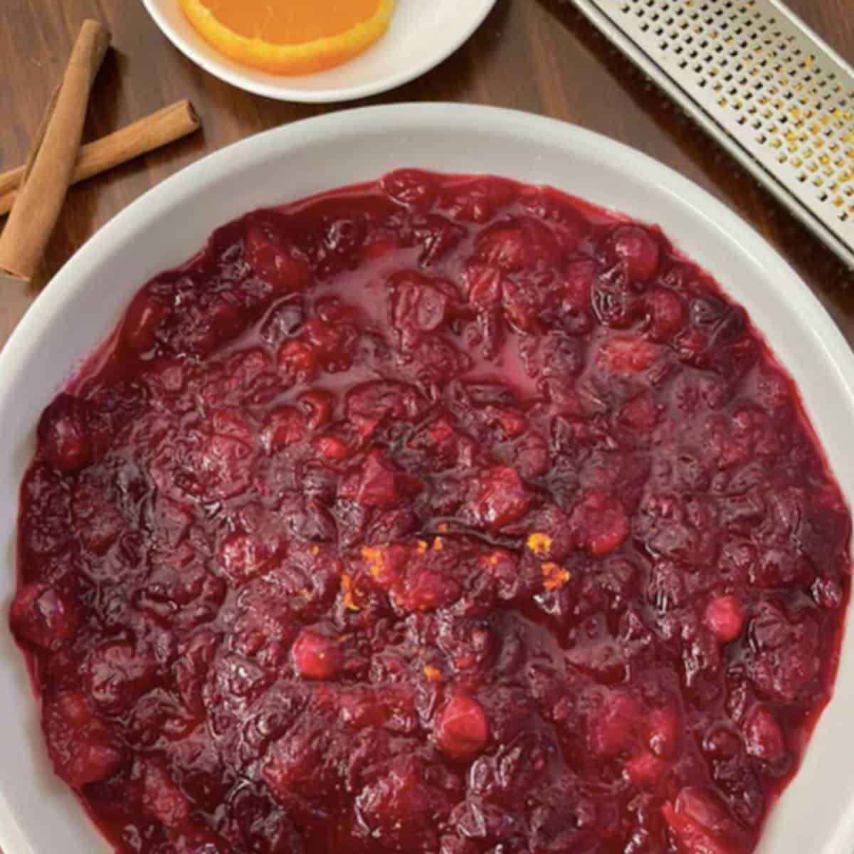Cranberry Sauce is bowl with orange and cinnamon on side.