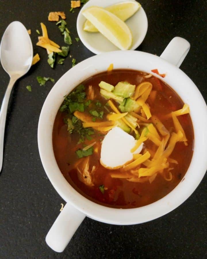 white bowl filled with chicken tortilla soup topped with cheese, tortilla strips, avocado and cilantro