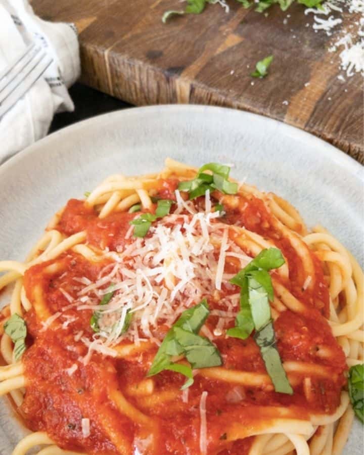 plate with bucatini and marinara sauce topped with basil and parmesan cheese