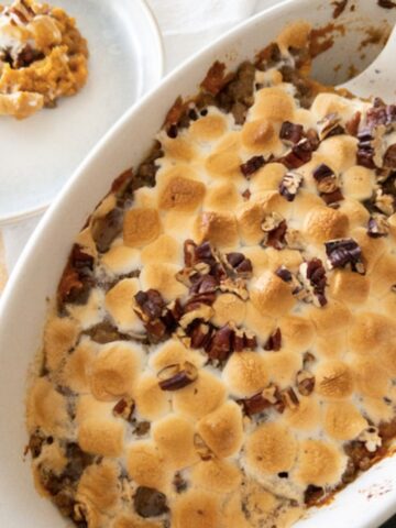 sweet potato casserole with toasted marshmallows and pecans in casserole dish with a plate with a helping