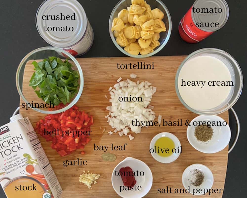 ingredients for creamy tomato spinach tortellini soup on cutting board with text