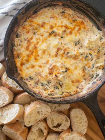 spinach artichoke dip in a cast iron skillet with bread on the side