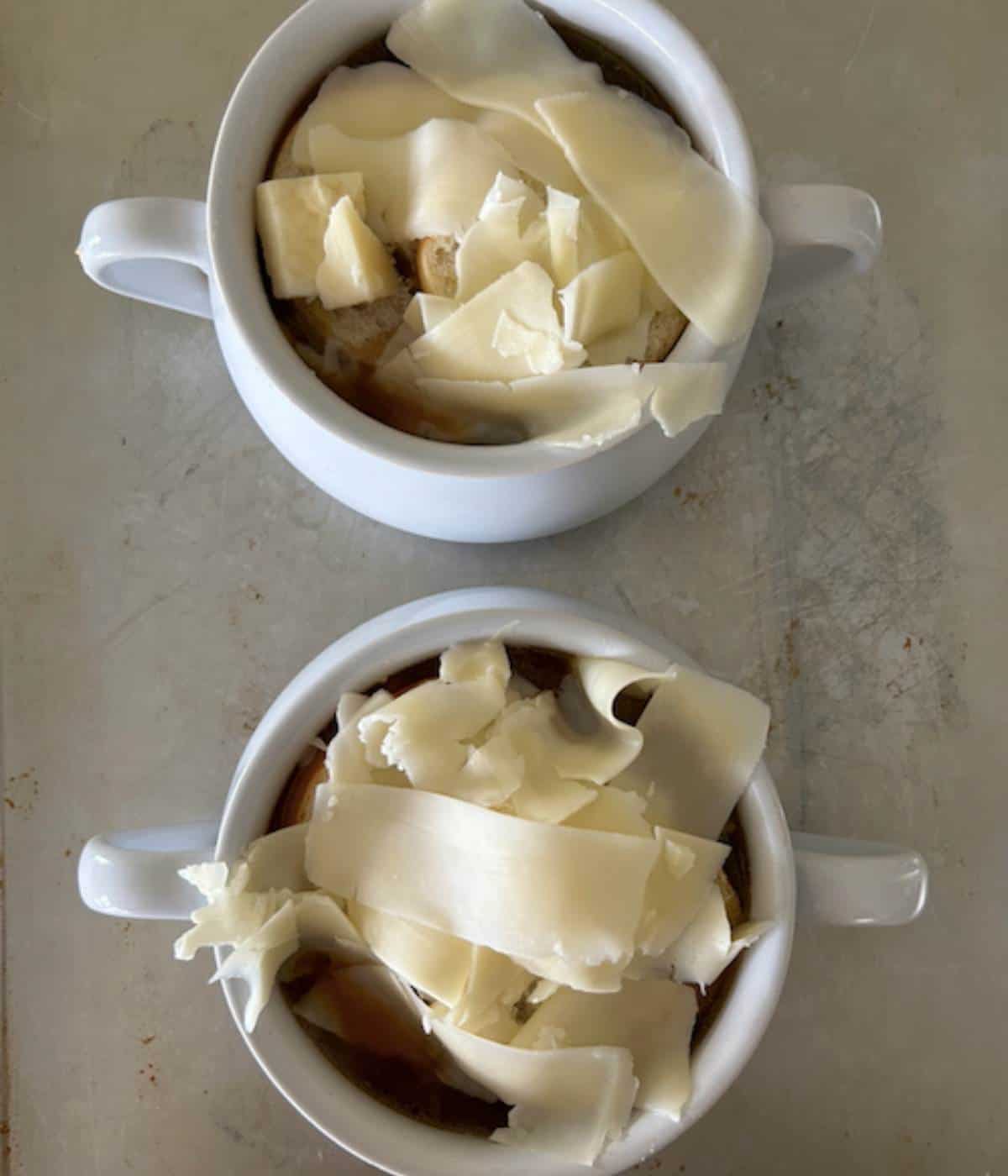 Two soup bowls full of French onion soup topped with bread and cheese.