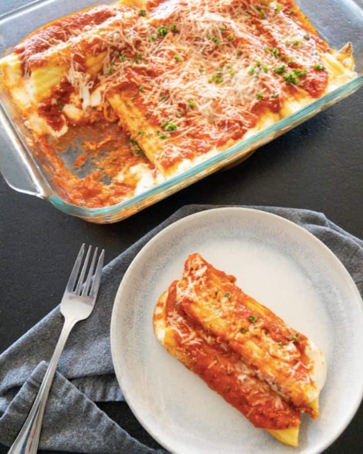 casserole dish full of manicotti with one serving plate with two manicotti covered in sauce and cheese