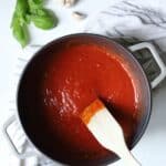 dutch oven full of marinara sauce with wooden spoon inside