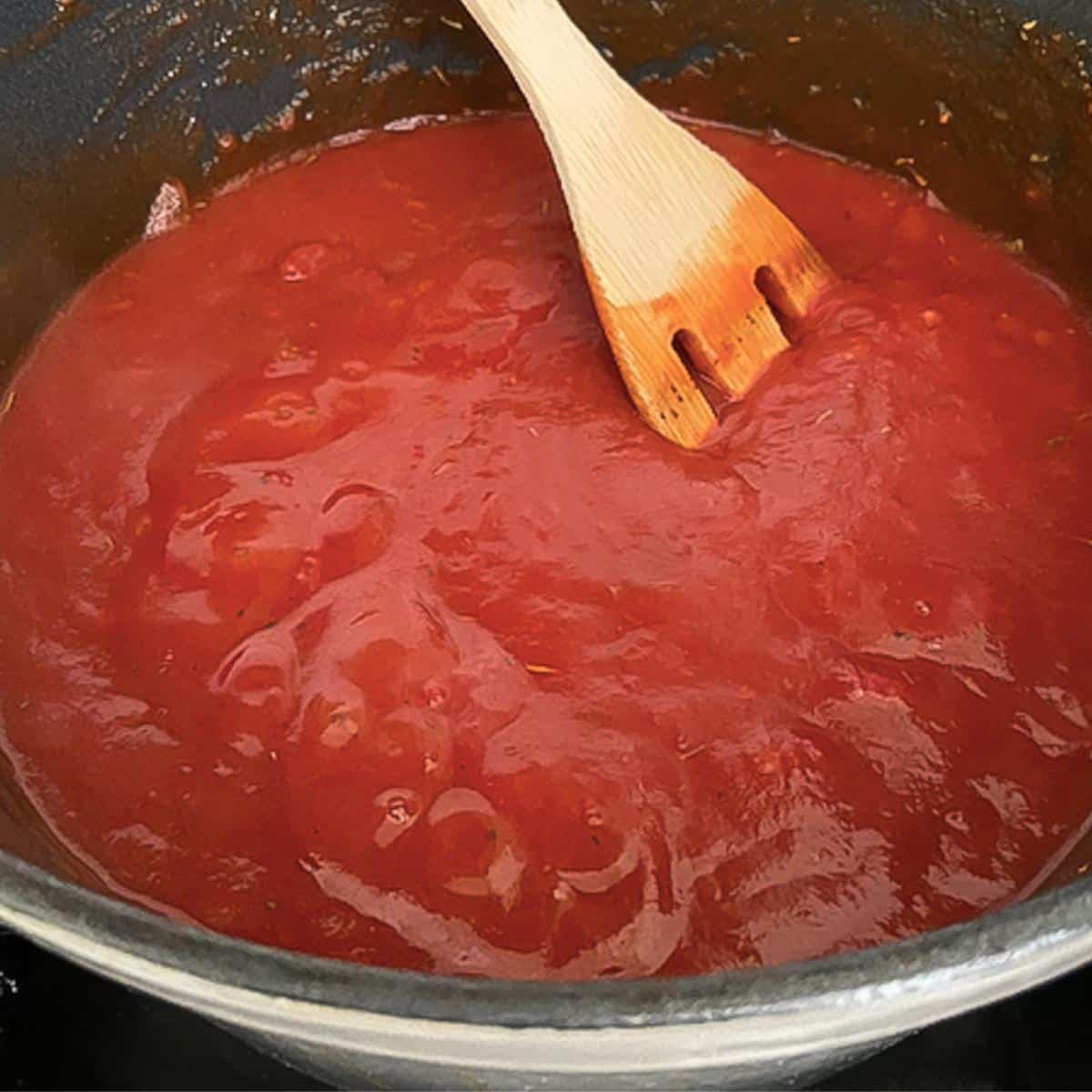 tomato sauce coming to a low boil with wooden spoon in pot