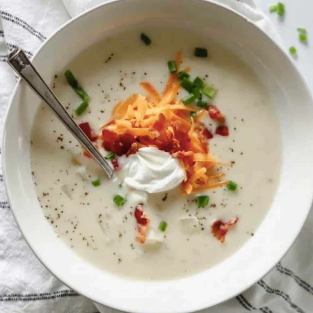Baked potato soup topped with sour cream, cheese and bacon in white bowl.