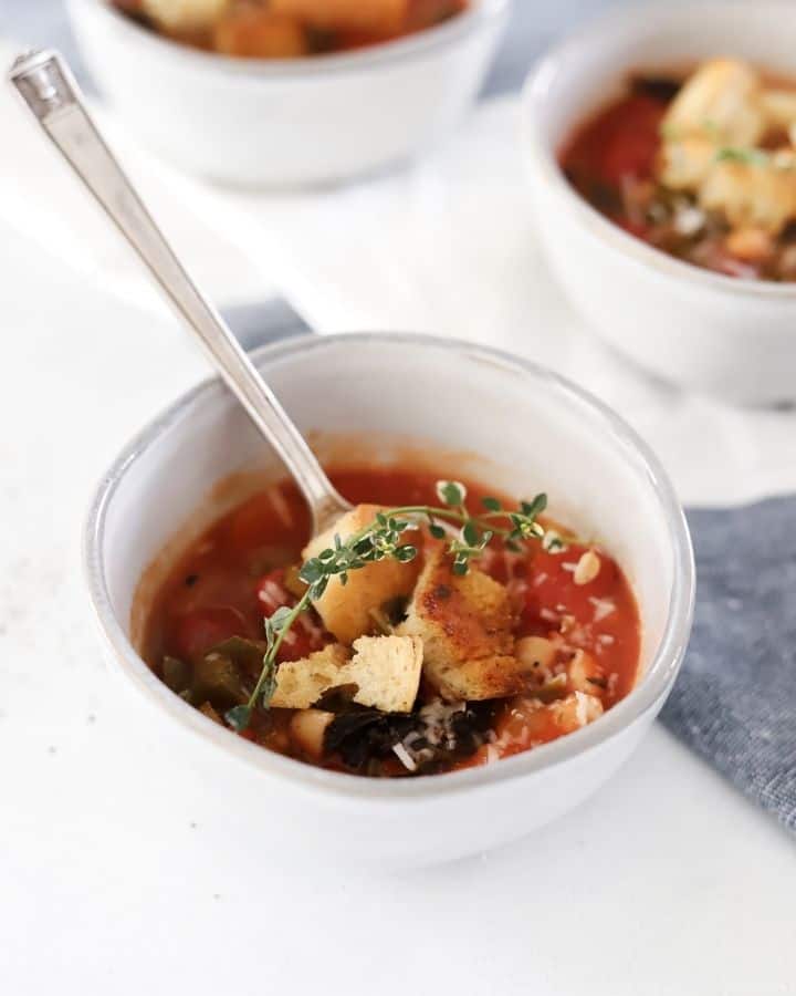chunky vegetable soup in a bowl with spoon topped with thyme sprig