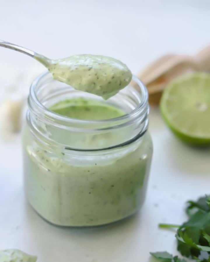 avocado cream sauce in jar with a spoon holding a serving