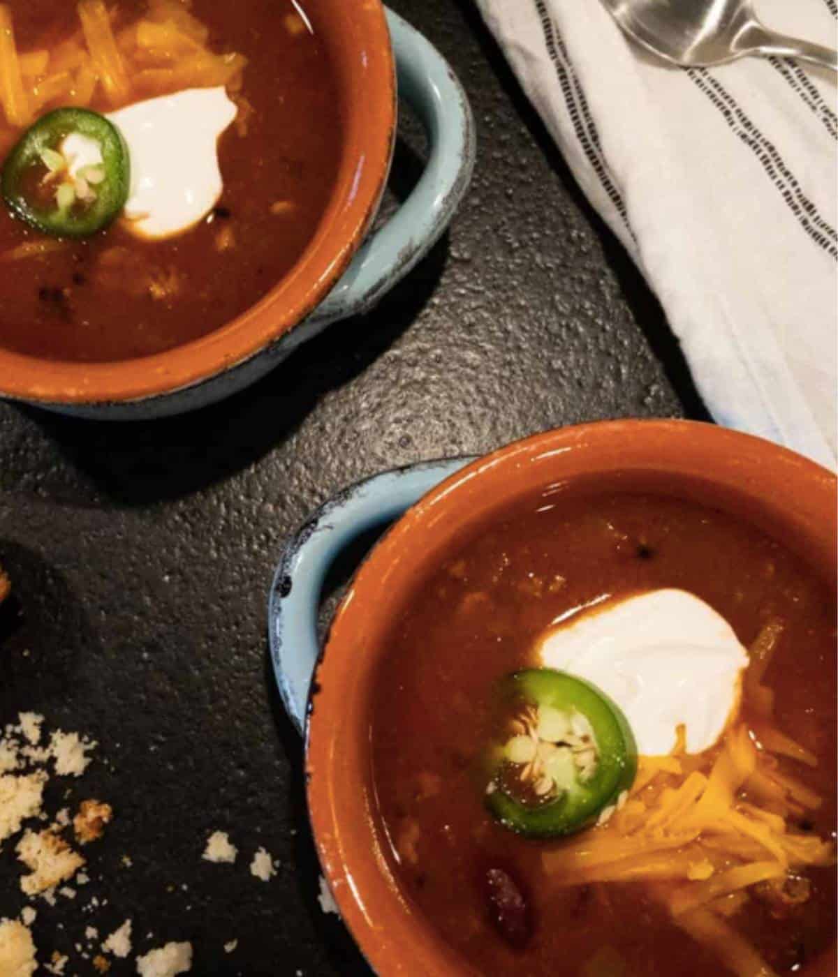 Chili in bowls topped with cheese, sour cream and jalapeno.