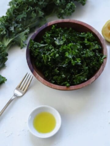 kale in a bowl with a side of olive oil and a lemon wedge