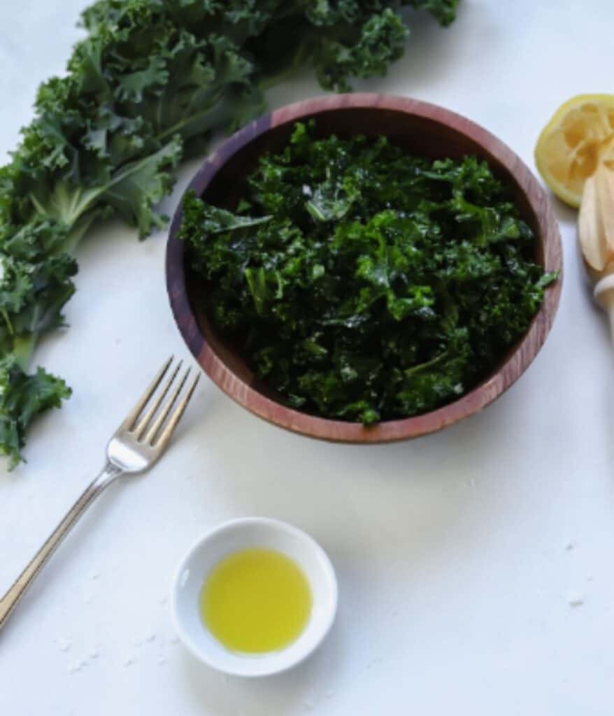 kale in a bowl with a side of olive oil and a lemon wedge