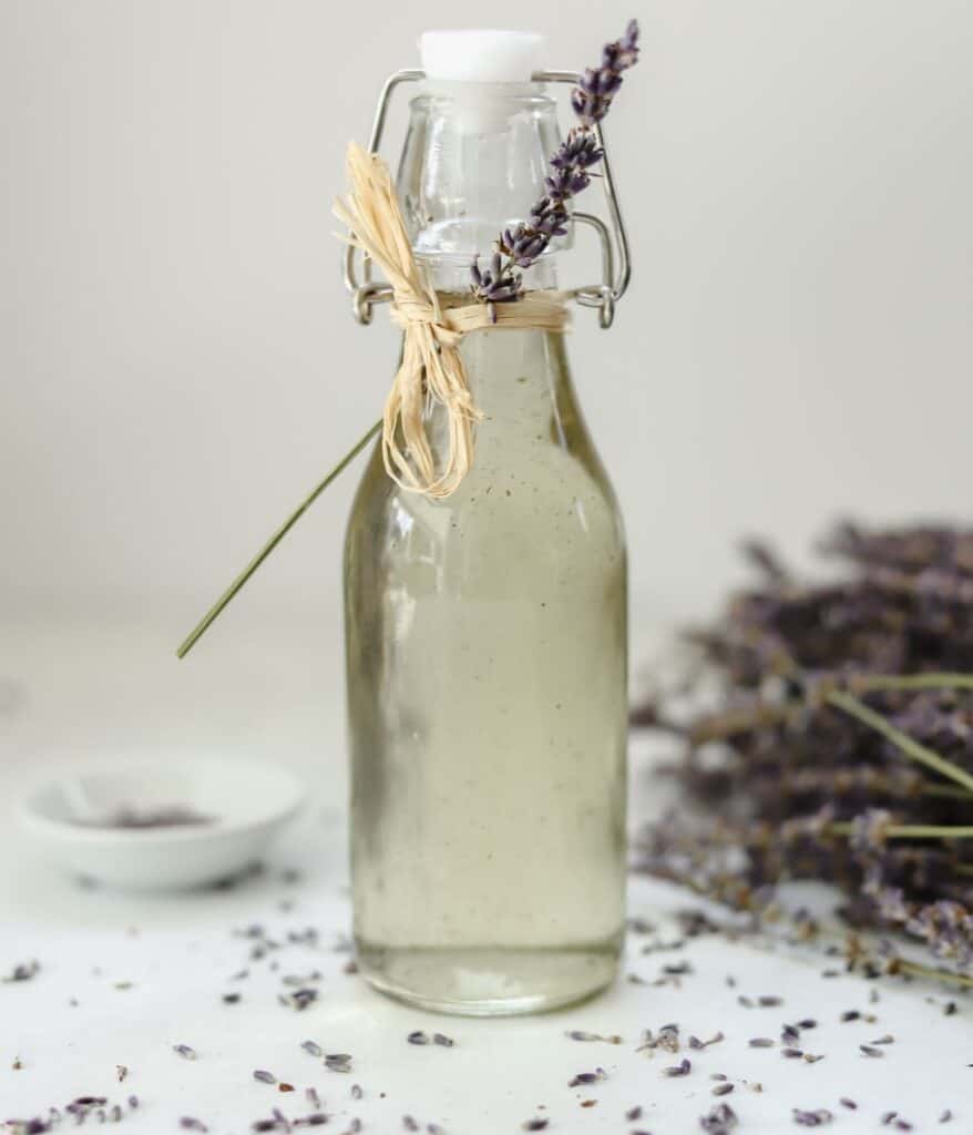Bottle of lavender simple syrup with fresh lavender in the background